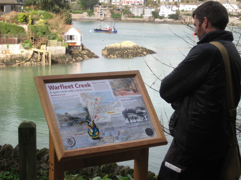 A visitor reading an interpretation panel with an oak lectern frame – the sign located by a river estuary