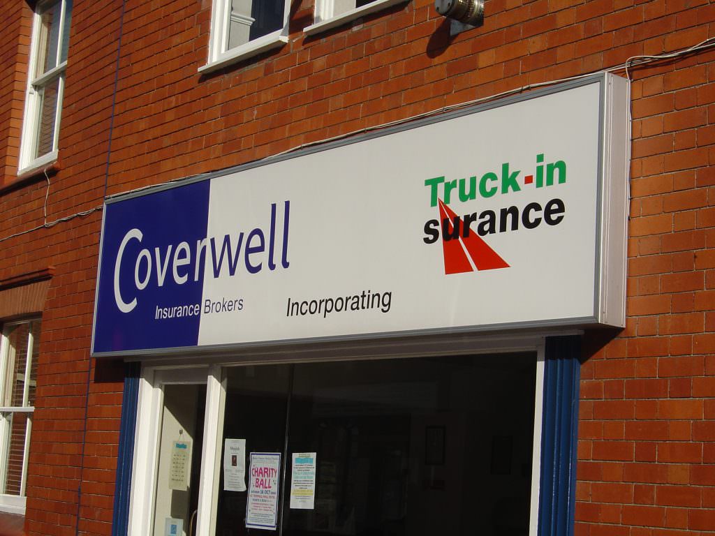 A large illuminated corporate entrance sign with a lighting box.  Full colour graphics and mounted on a brick wall above the shop door